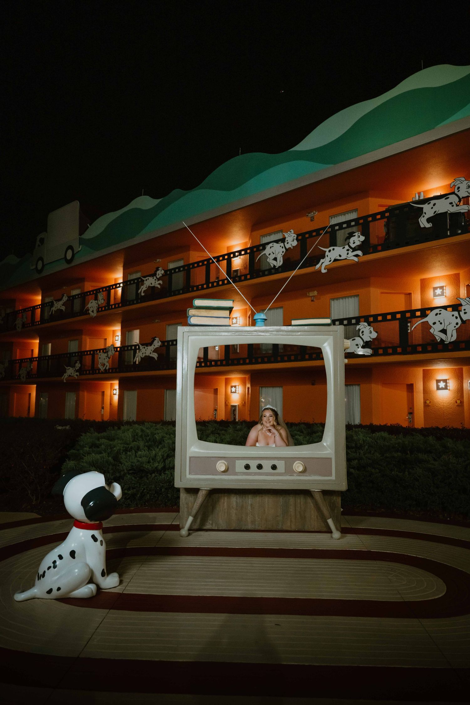 Child poses inside a giant vintage TV prop at Disney's All-Star Movies Resort at night with Dalmatian decor.