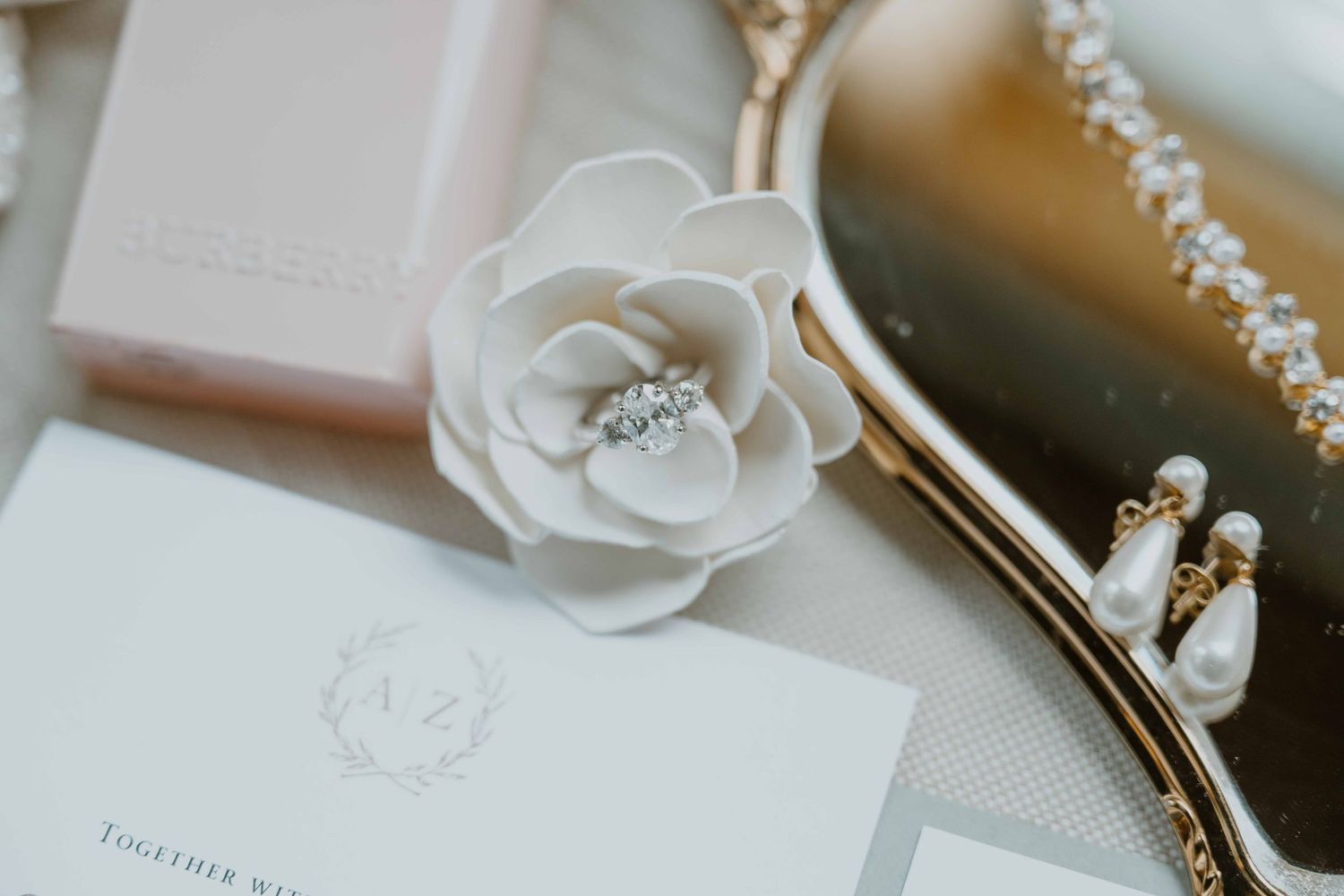 Elegant wedding flat lay with floral hair piece, pearl clutch, diamond earrings, and monogrammed invitation.