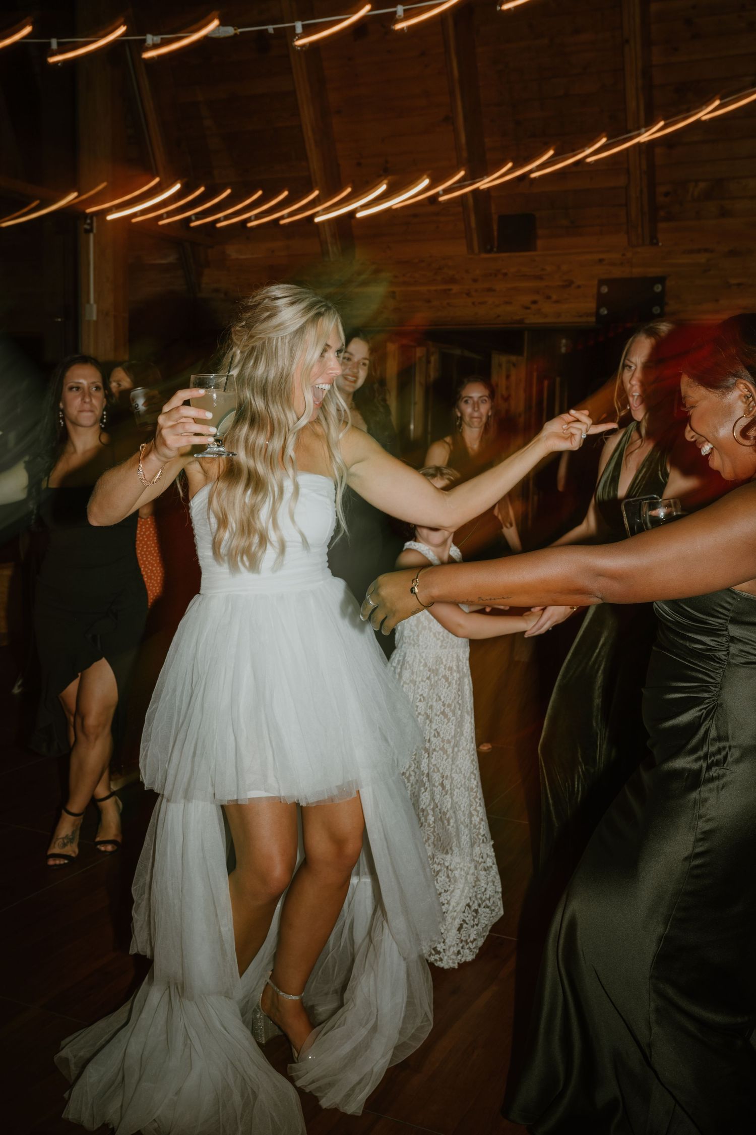 Bride in white tulle dress laughing while dancing with guests at wedding reception.