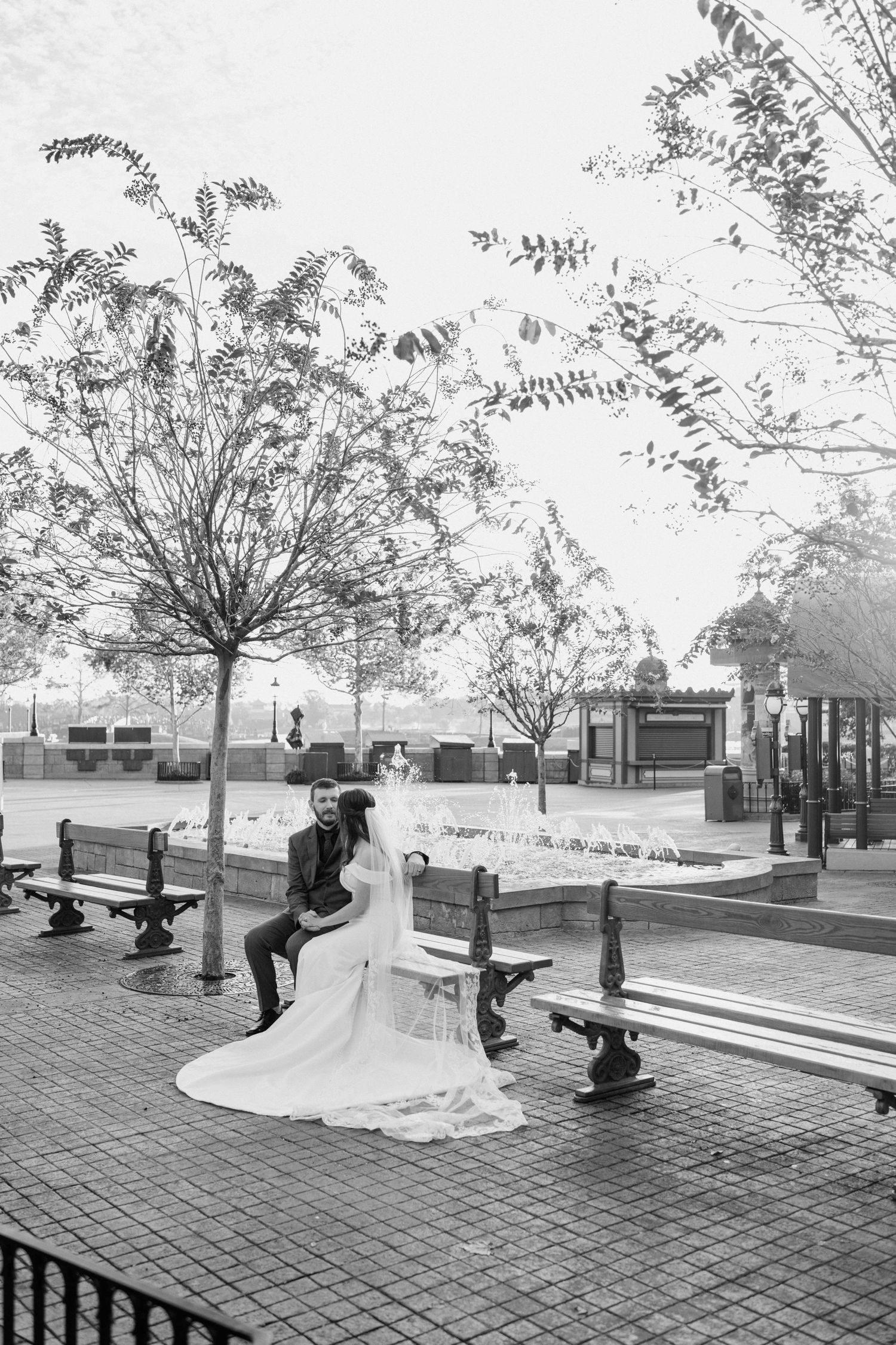Black and white photo of newlyweds sitting on a bench in a park plaza during their Disney wedding.