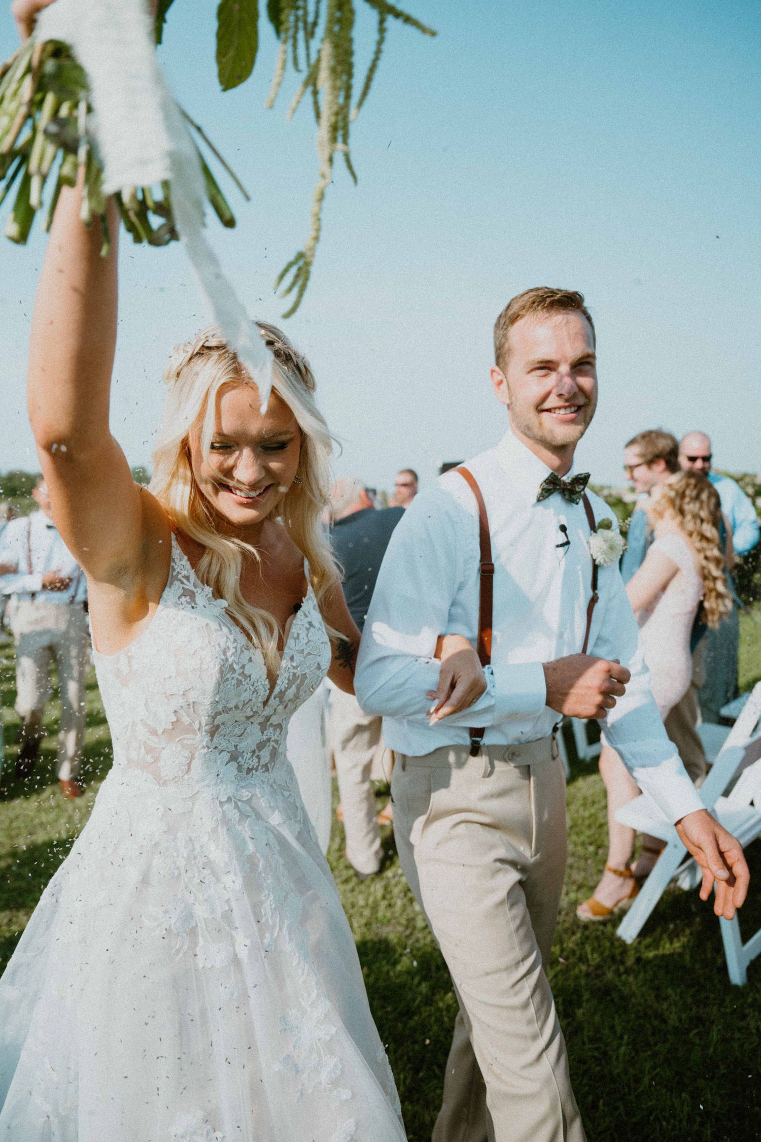 Elated newlyweds walking back down aisle as bride raises bouquet in celebration after outdoor ceremony.