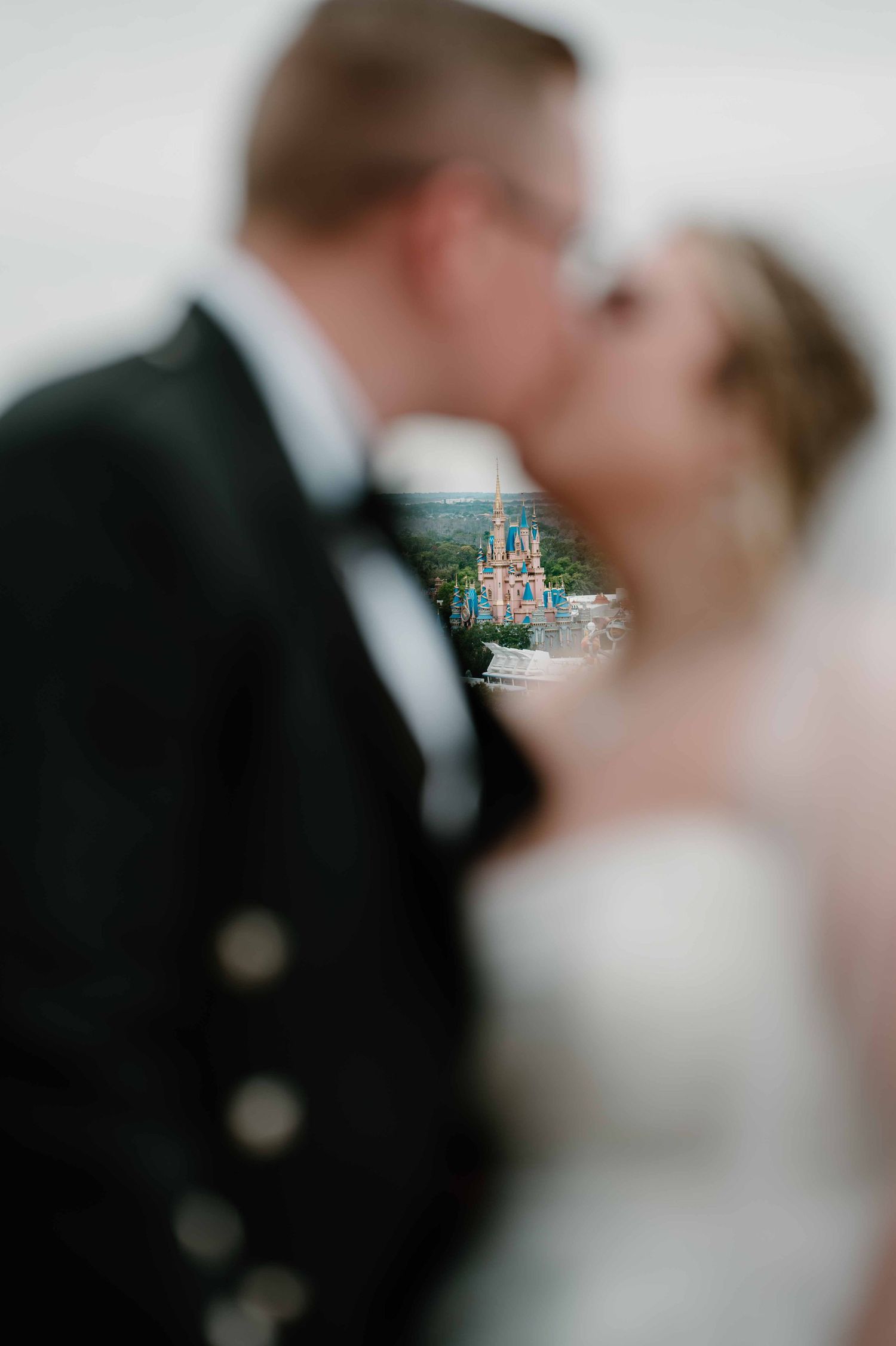 Bride and groom kissing with Cinderella Castle visible between them at Disney World wedding.