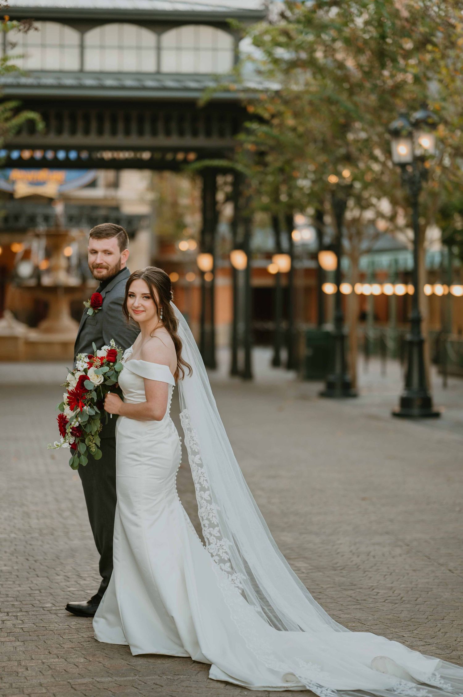 Elegant bride in a fitted gown with cathedral veil stands with groom at a Disney theme park wedding.