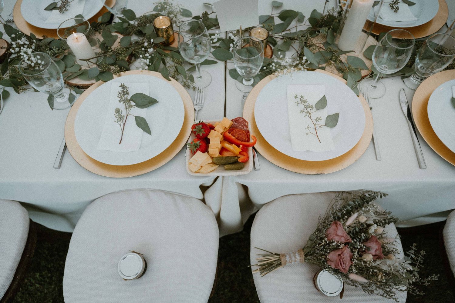 Elegant wedding reception table with gold-rimmed plates, greenery runner, and botanical place cards.