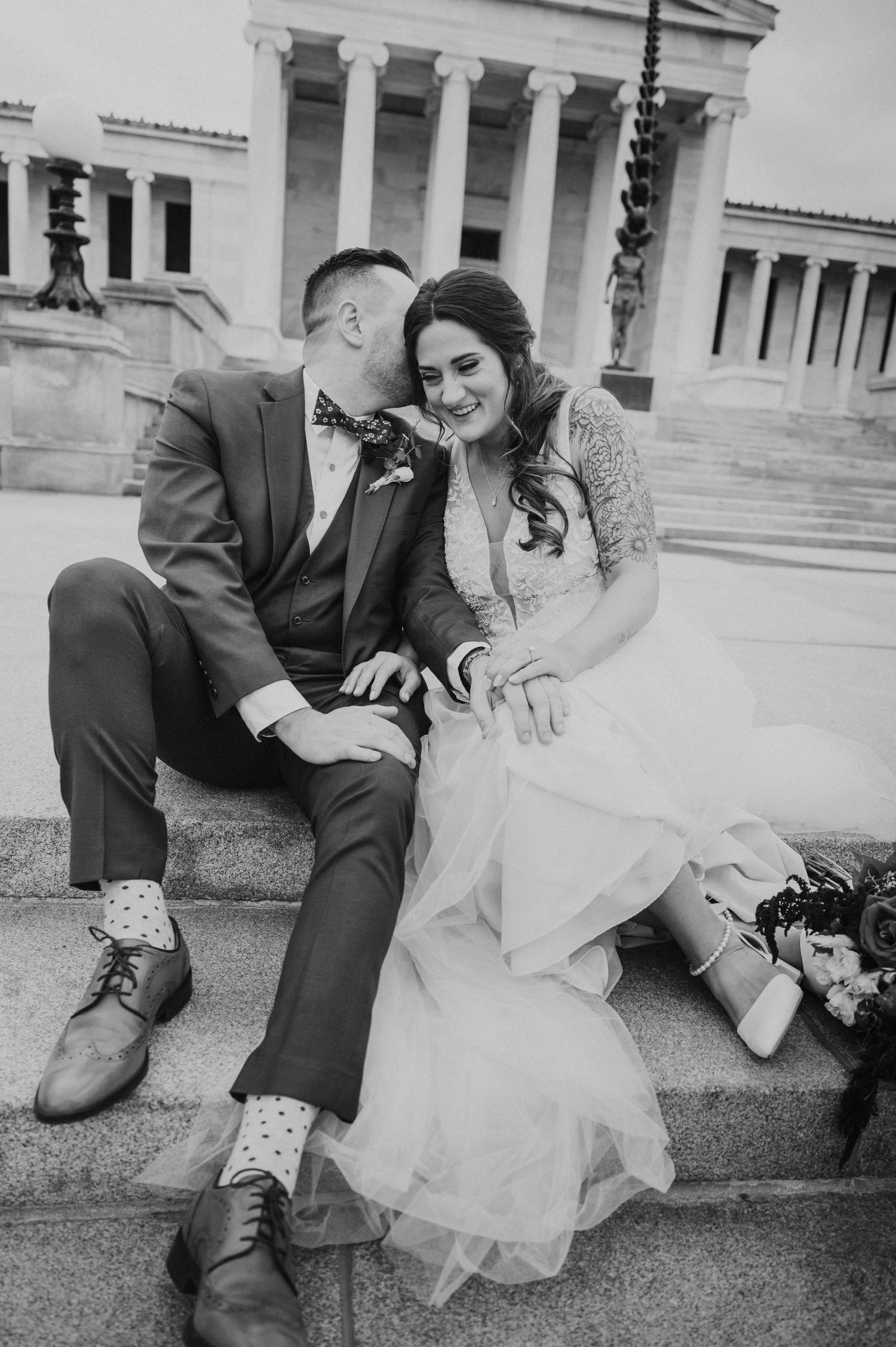 Black and white photo of bride and groom laughing together on steps of classical building.