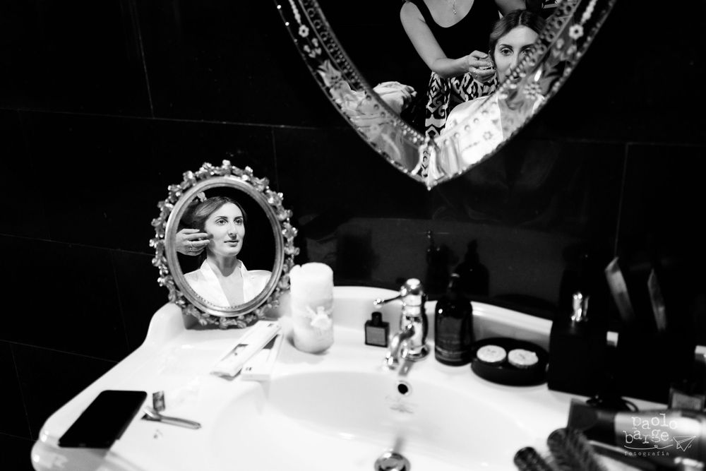 Black and white image of a vanity table with bottles and glassware with vintage mirrors reflecting light.