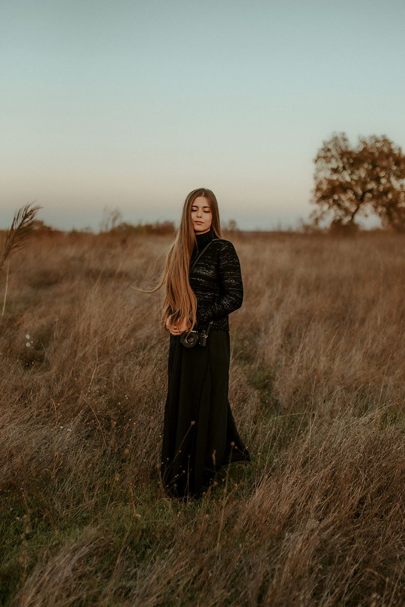 Woman in black dress standing in golden autumn field at dusk.