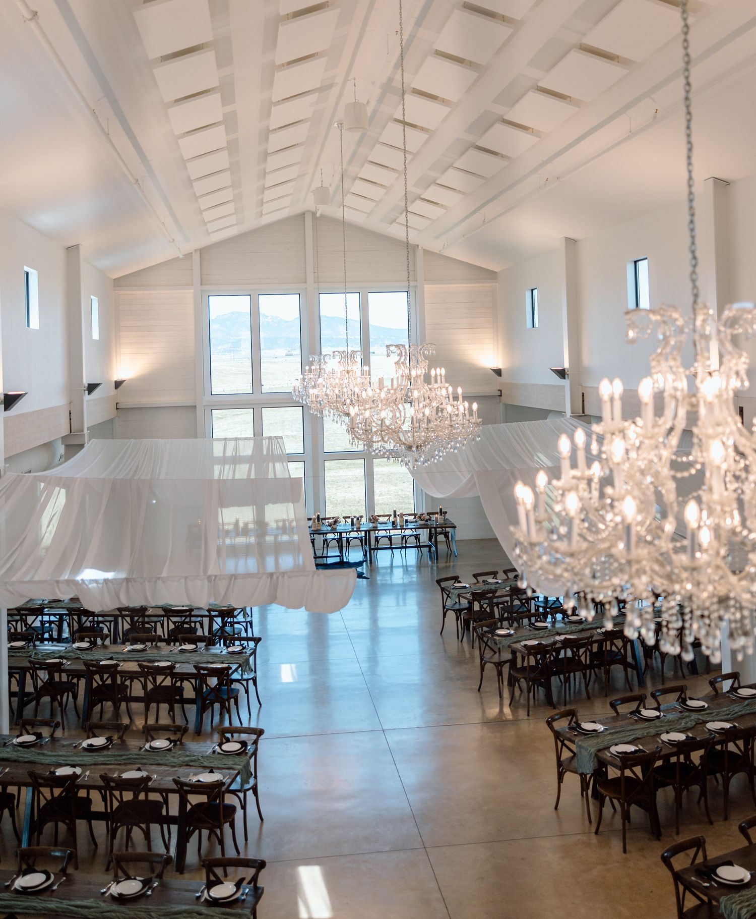Spacious wedding reception hall with crystal chandeliers and dark wooden chairs.