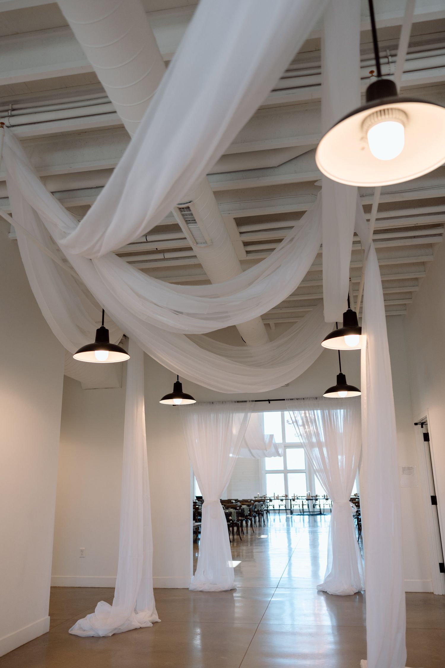 Modern white venue space with flowing fabric drapes and industrial pendant lights.