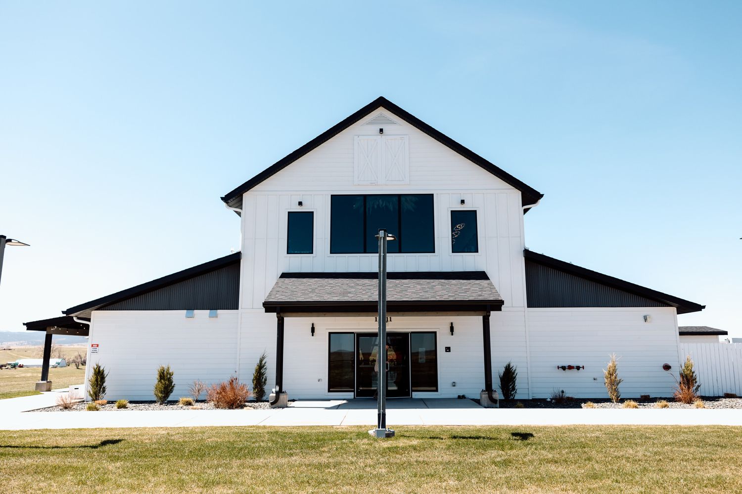 Modern white farmhouse exterior with black trim sits against a scenic rural landscape.