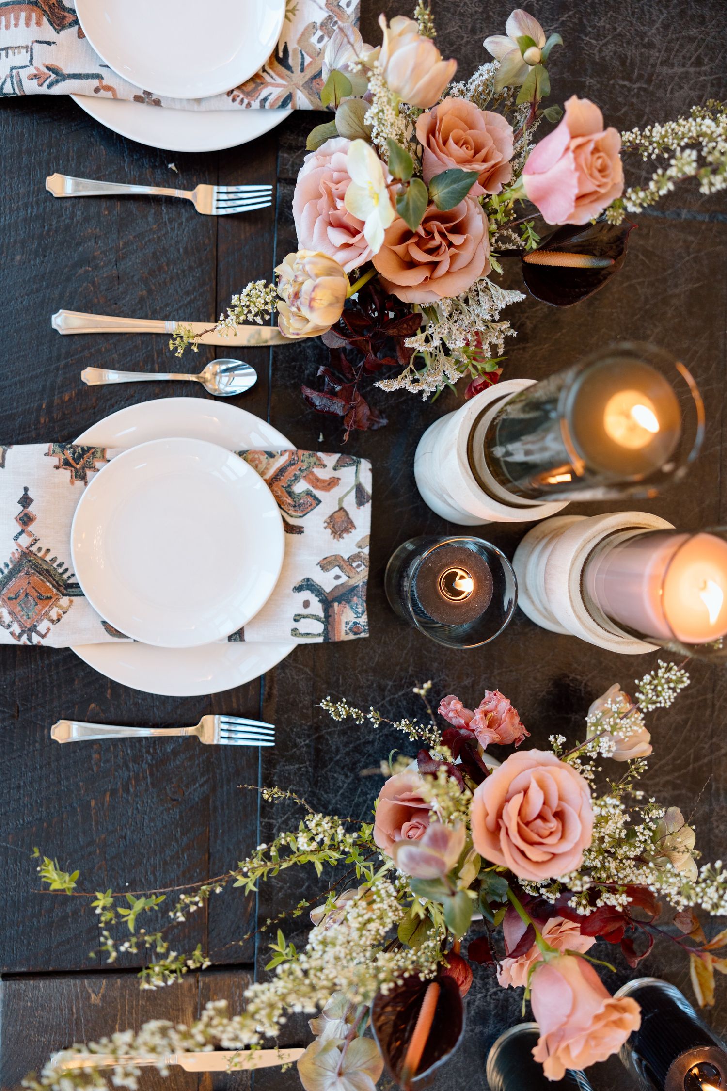 Wedding table decor with pink roses, white plates, and glowing candles.