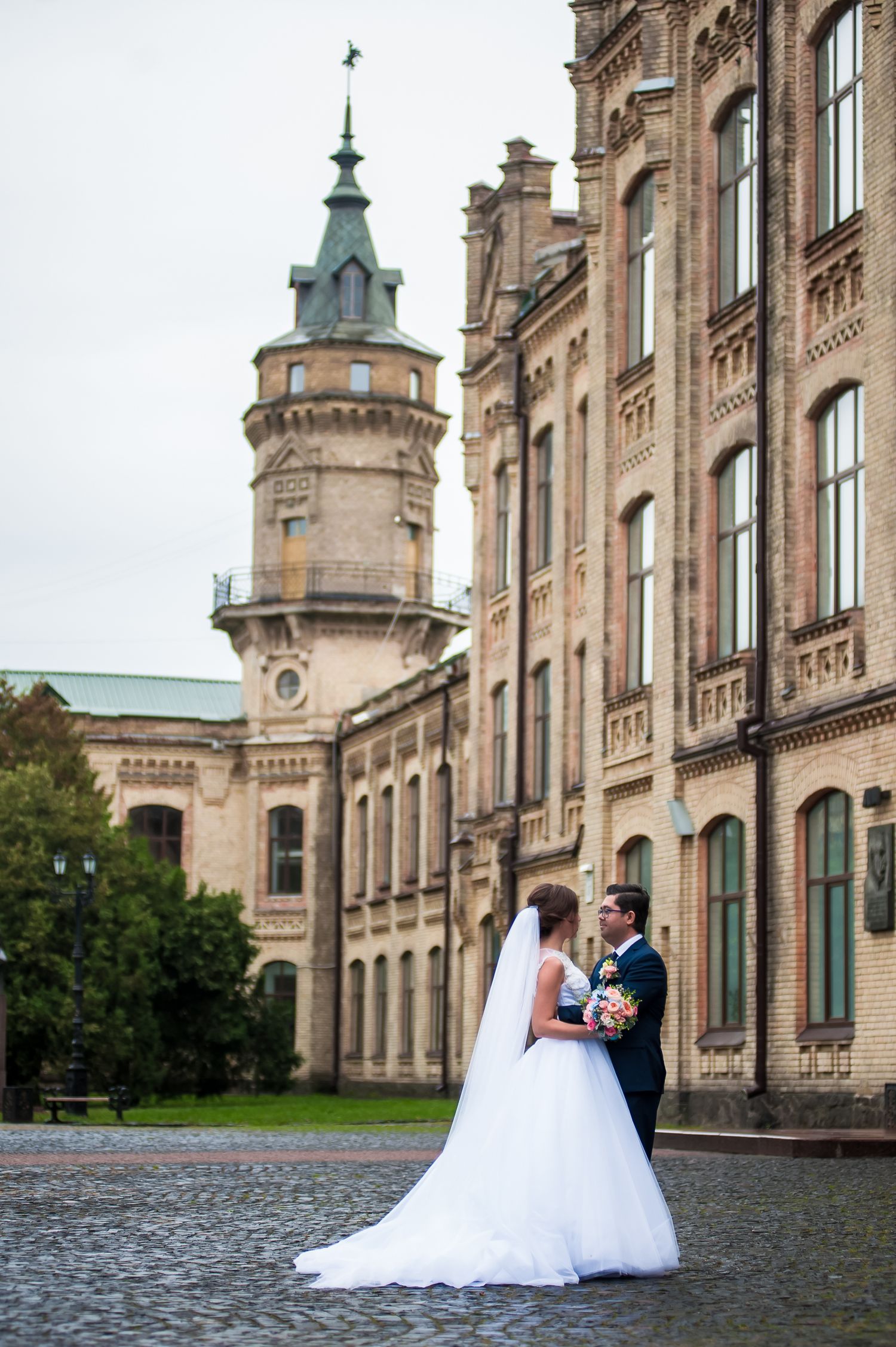 A romantic wedding portrait in front of historic architecture with ornate tower and cobblestone ground.