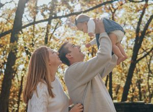 A family shares a joyful moment together under autumn trees during an outdoor photoshoot.