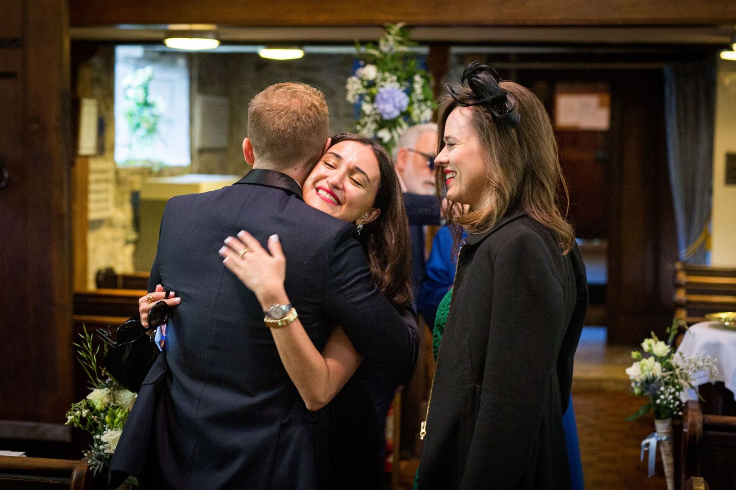 Wedding celebration with guests embracing in a warmly lit indoor venue.