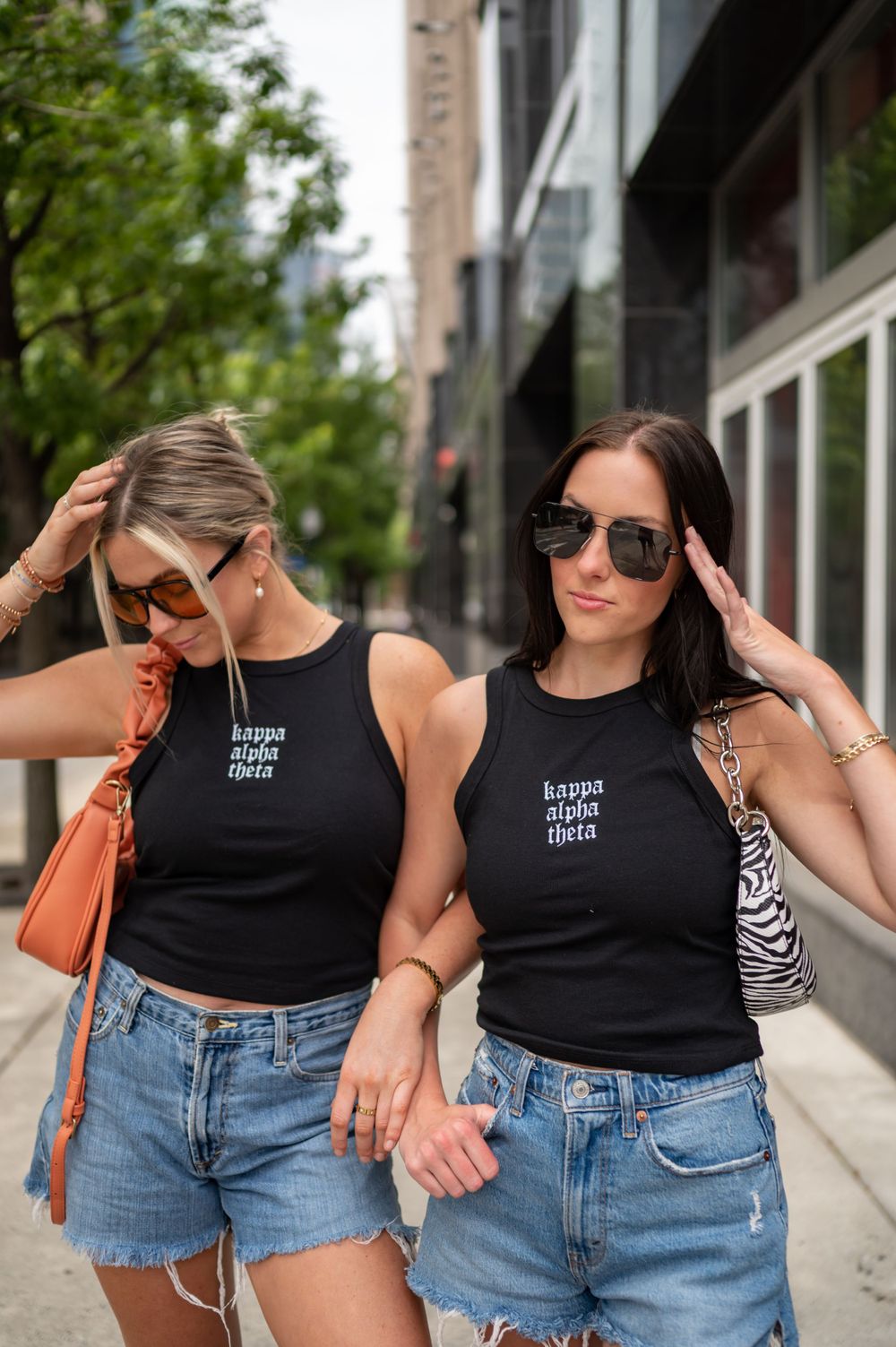 Two women in matching black tank tops and denim shorts posing on a city street.