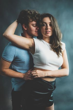 A young couple embraces intimately in a moody studio portrait with dramatic lighting.