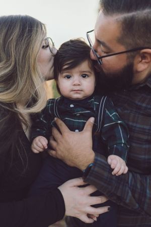 Parents kissing their baby on the cheeks during an outdoor family portrait session.