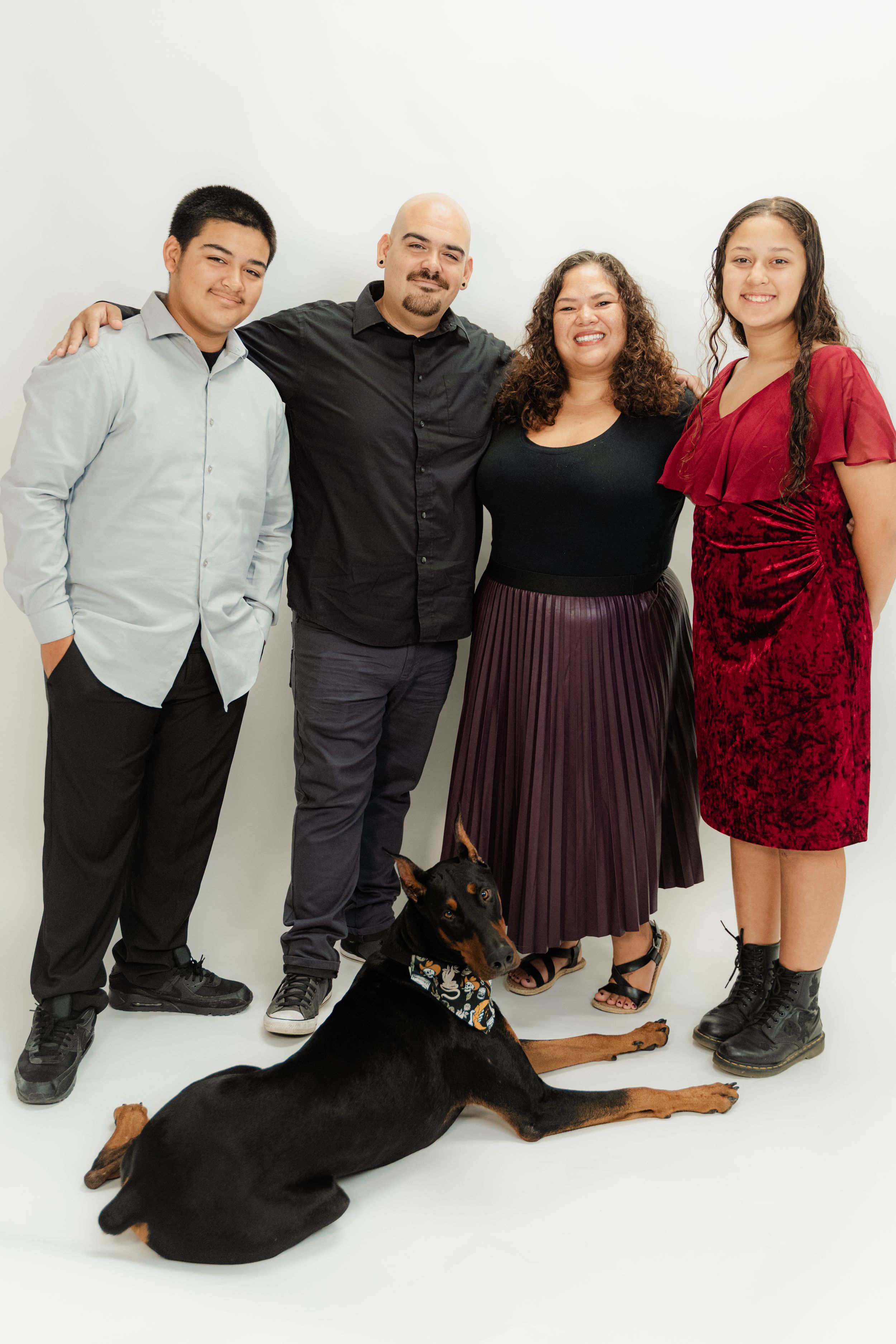 Family of four smiling with a Doberman dog during a white background studio portrait session.