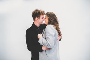 A young couple in casual winter clothing share a romantic moment against a white background.