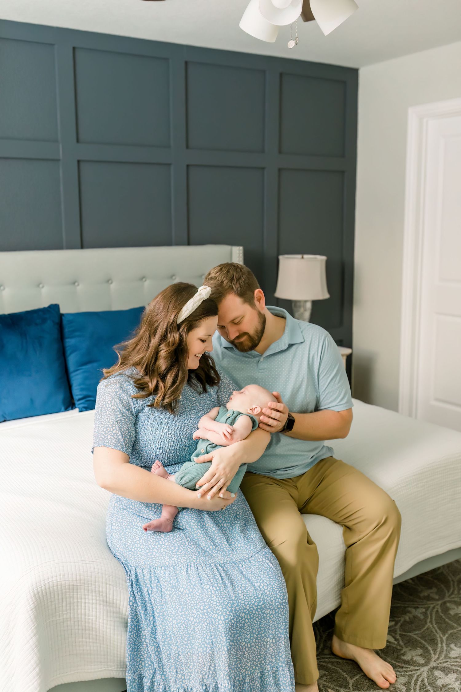A touching family moment captured on a bed with sage green walls and blue pillows in the background.