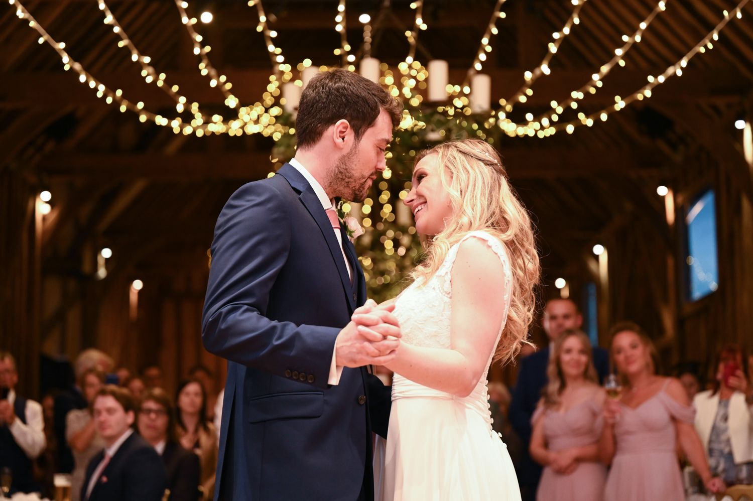 First dance under twinkling lights at rustic barn wedding reception.