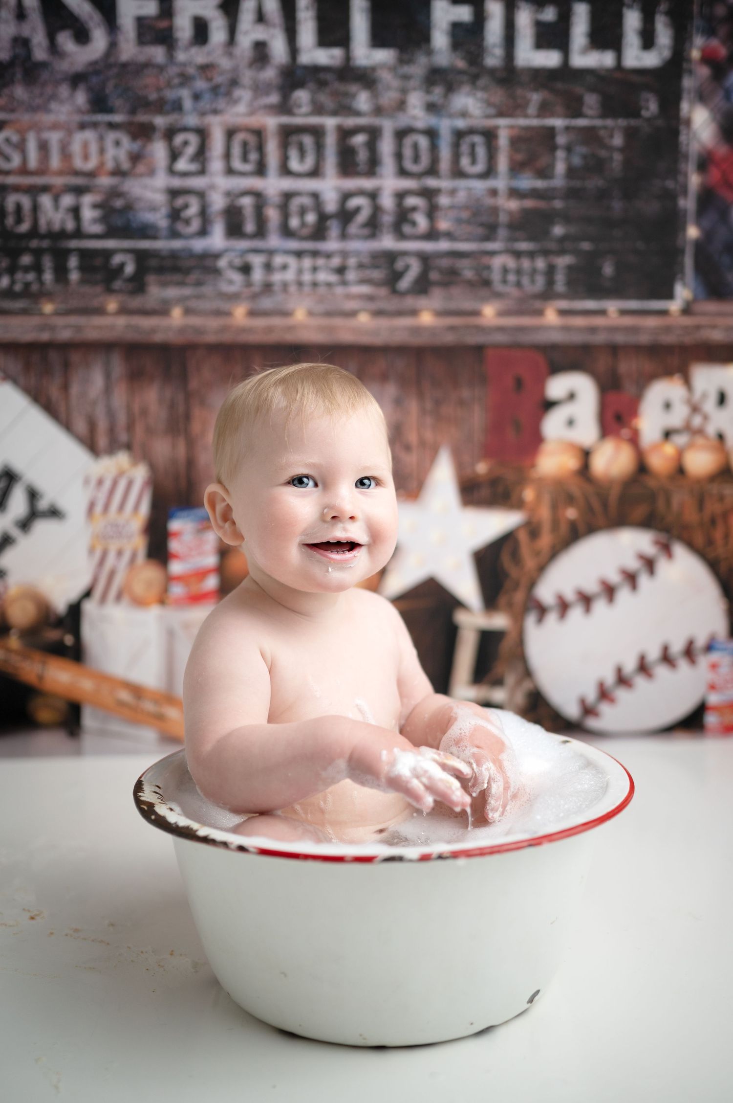 Baby sits in vintage white enamel basin during baseball themed photo session.