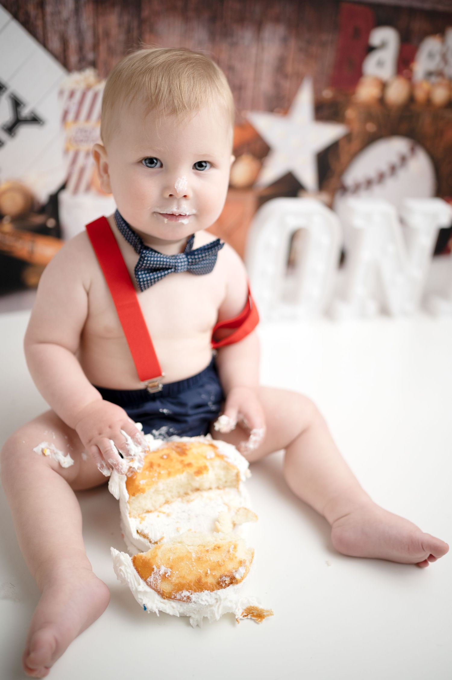 Baby in bow tie smashes cake during first birthday photoshoot with festive background.