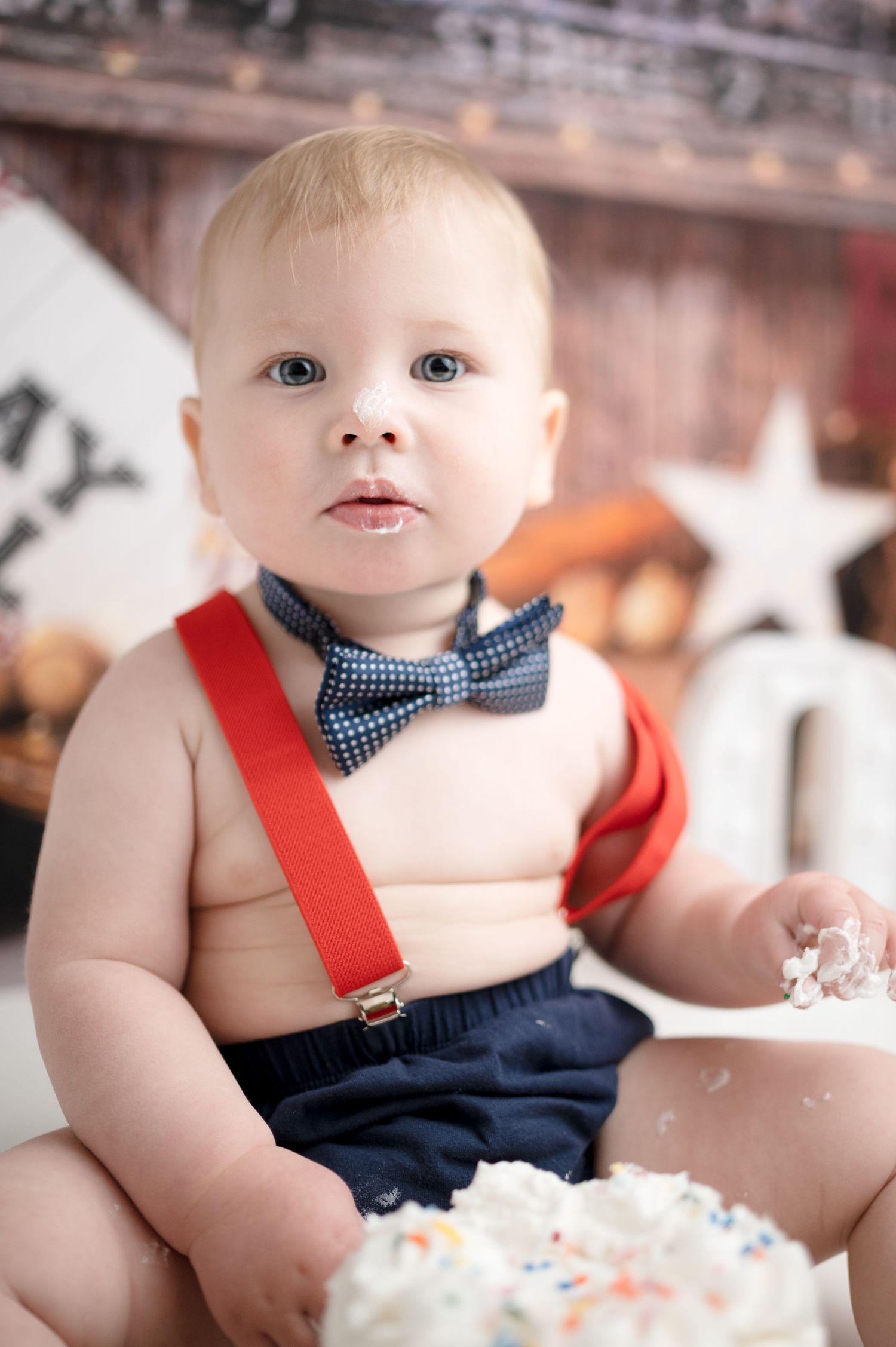 Close up of baby wearing suspenders and bow tie during baseball themed cake smash photo session.