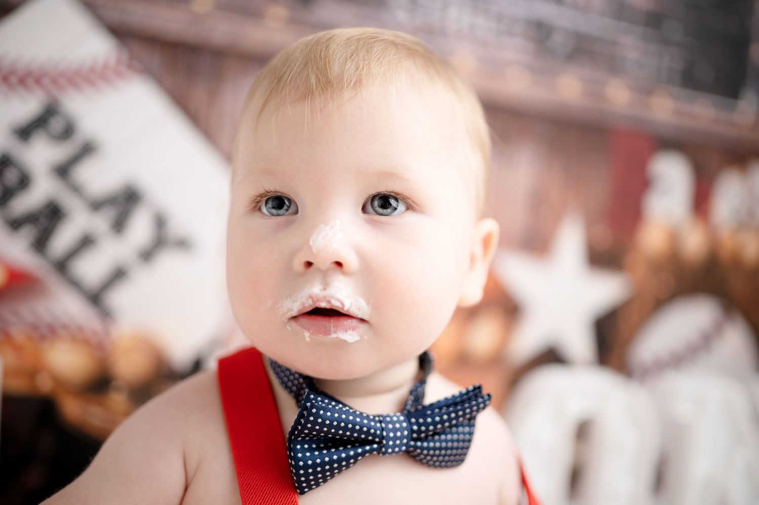 Baby in navy outfit with red suspenders poses during baseball themed photoshoot.