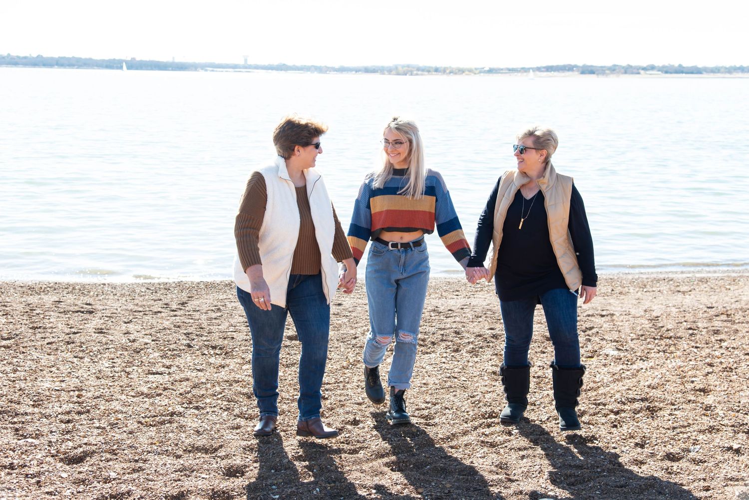 Three friends walking together along a beach shoreline on a sunny day.