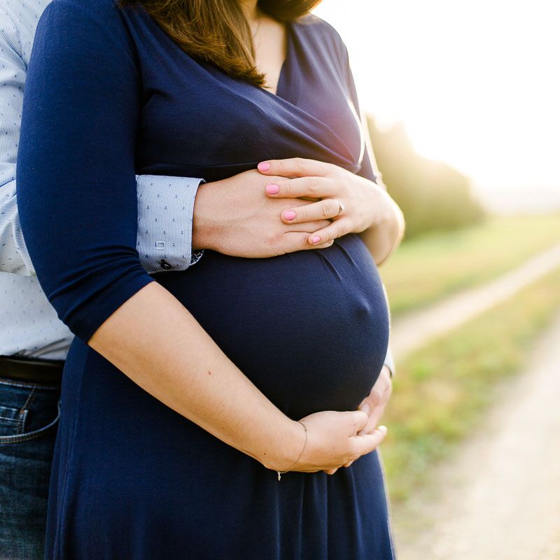Babybauch-Fotoshooting, Hände berühren den rundem Babybauch, Nahaufnahme im Profil