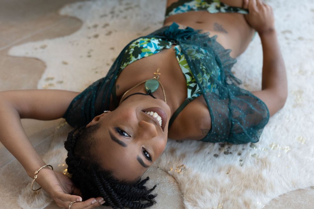 woman in a Sultry forest green 3 piece lingerie set laying ion the floor with a big smile at her boudoir session