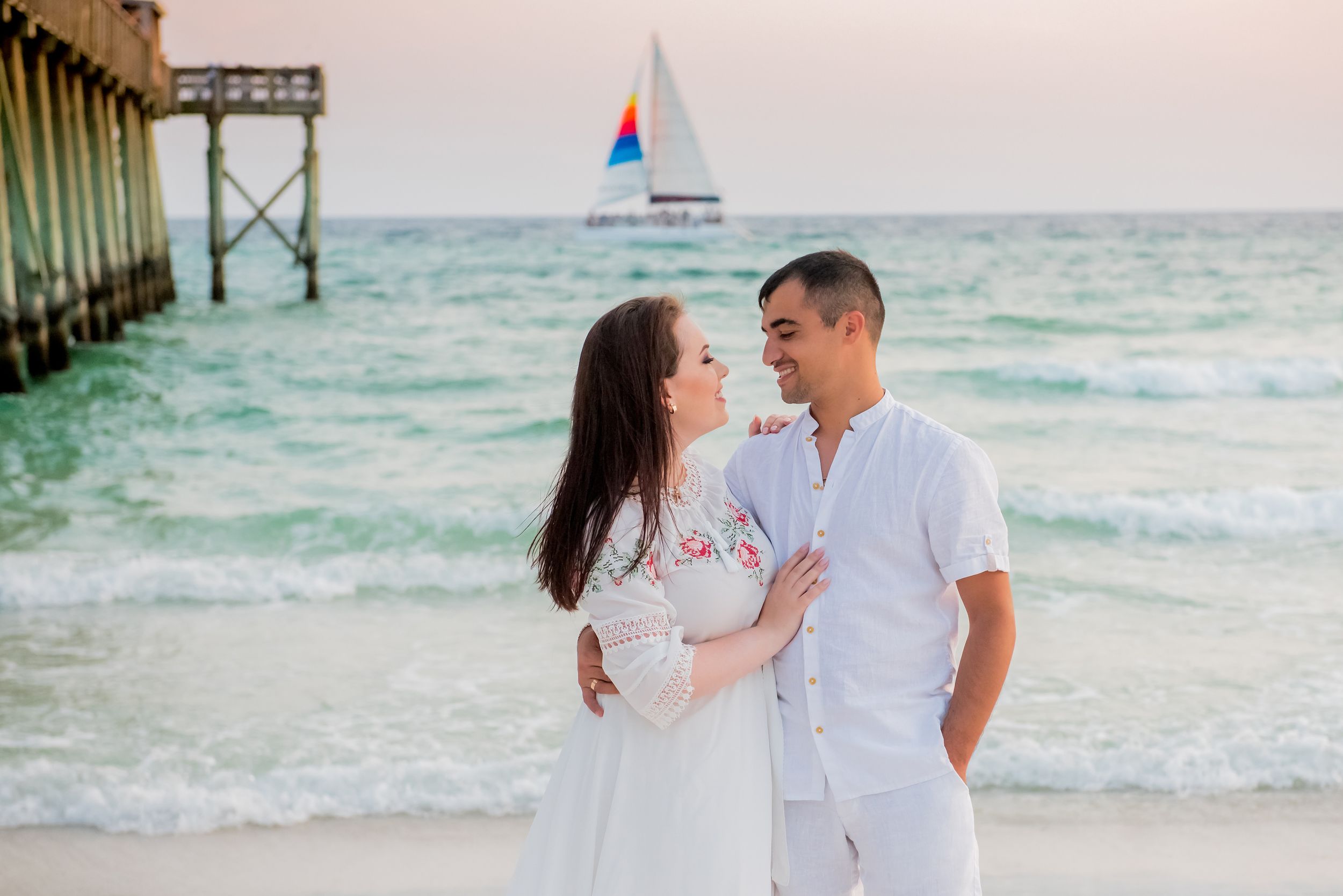 couple embracing during family beach portrait session at sunset with sailboat on Panama City Beach Florida