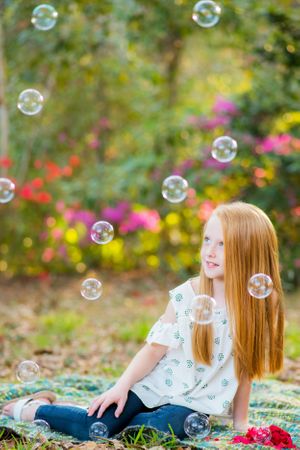 little girl looking at bubbles with flowers in background during portrait session in Panama City Florida