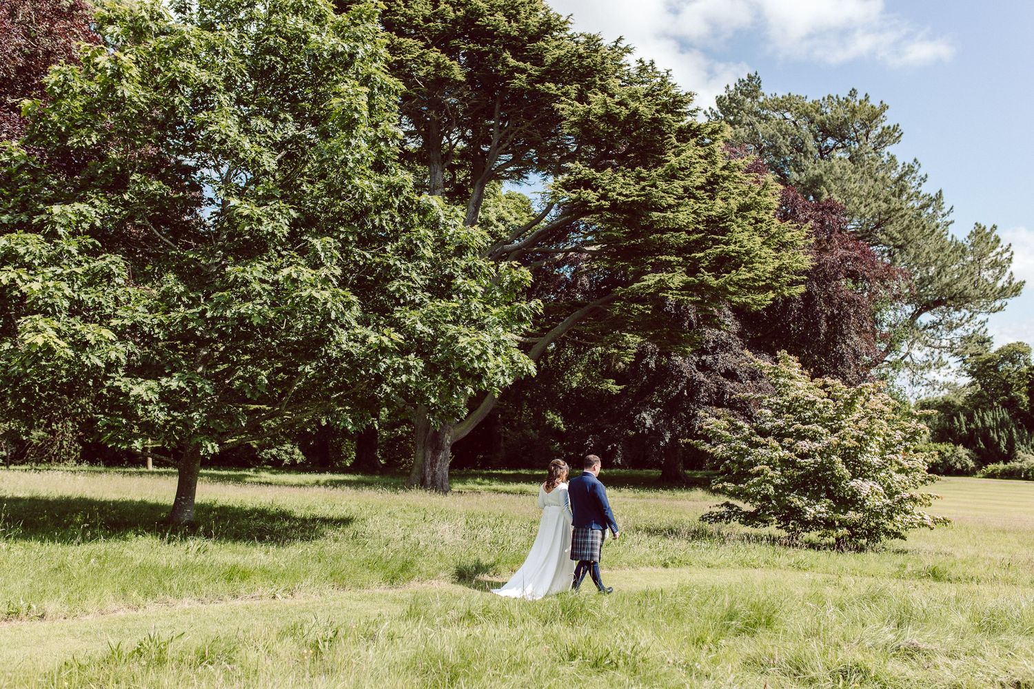 Bride and groom walking near trees in the sunshine