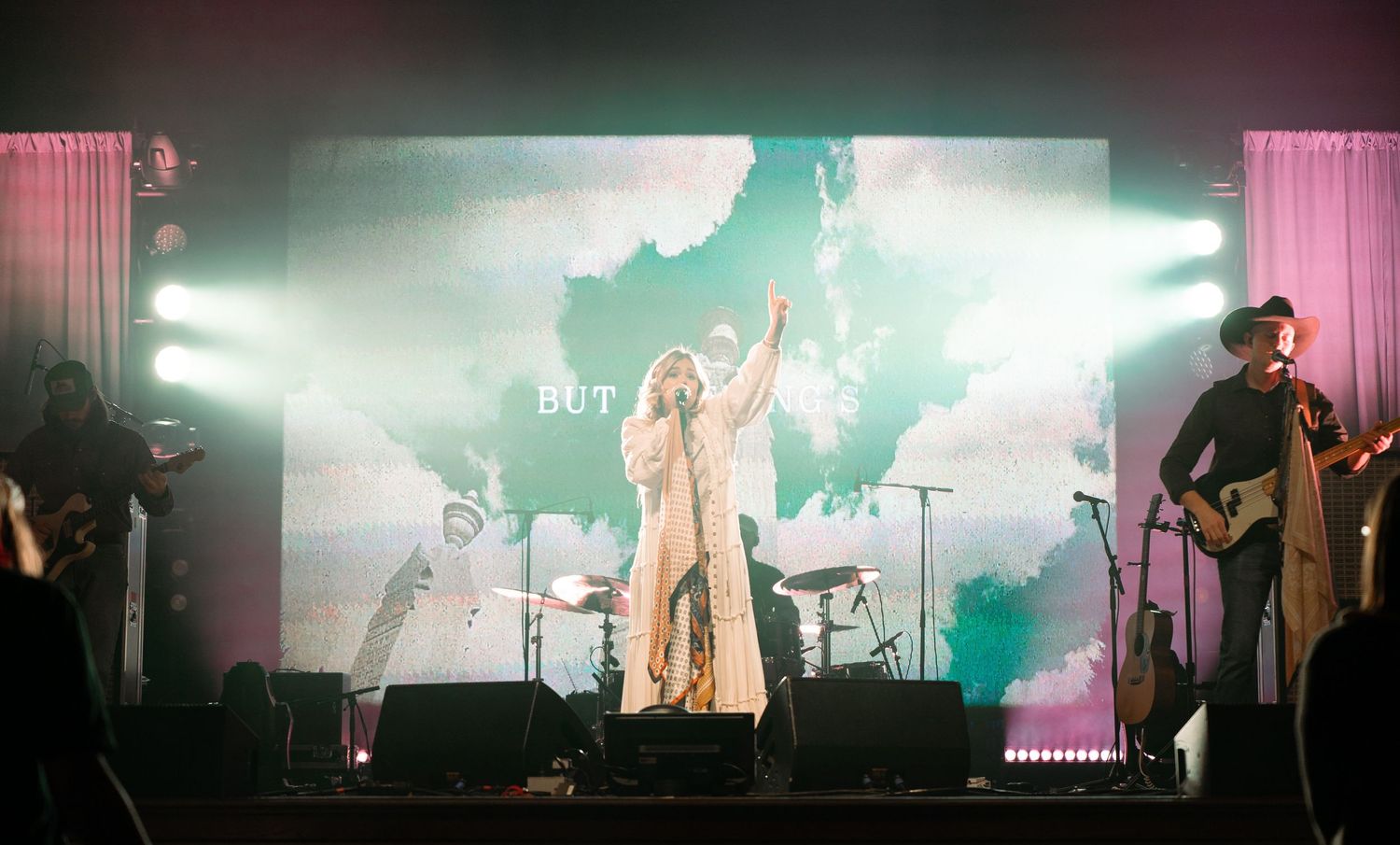 woman singing on stage with a large led wall behind her and lights shining all around