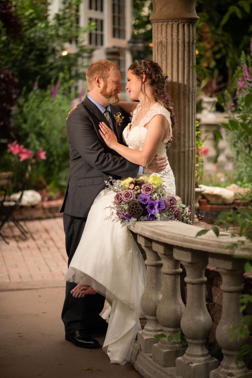 A romantic wedding portrait by stone pillars surrounded by blooming garden flowers.