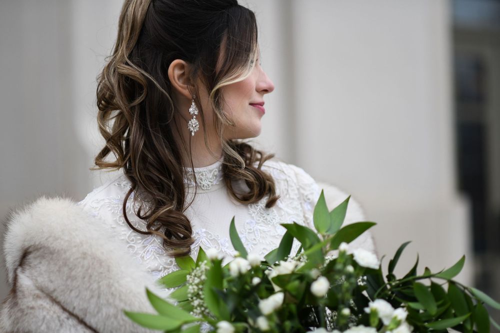 A side profile view of a bride in winter wearing a fur shawl and holding a white and green bouquet.