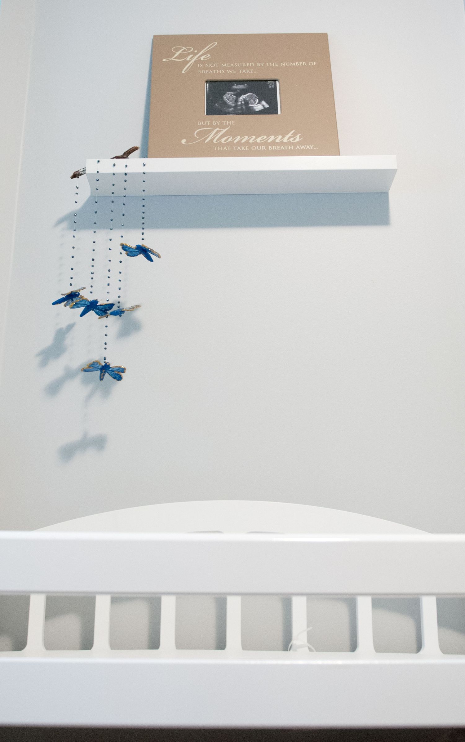 White crib with delicate blue hanging mobile and life moments photo album above.