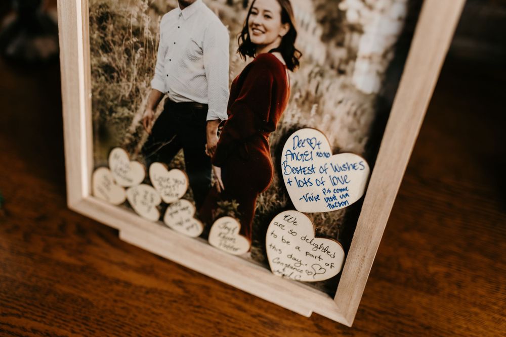 Close-up of wedding guest book frame with couple photo and wooden heart signatures from wedding guests.