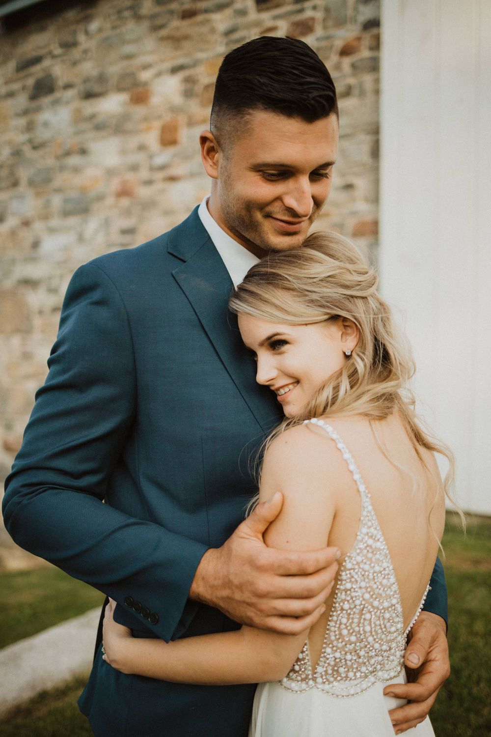 Intimate portrait of a couple embracing against a rustic stone wall at sunset.