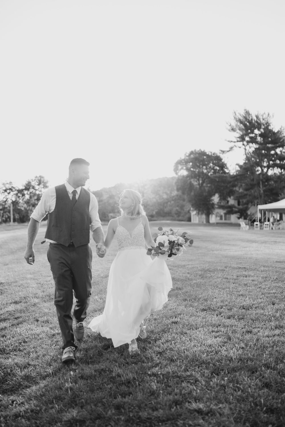 A black and white photo of a couple walking through a grassy field on their wedding day.