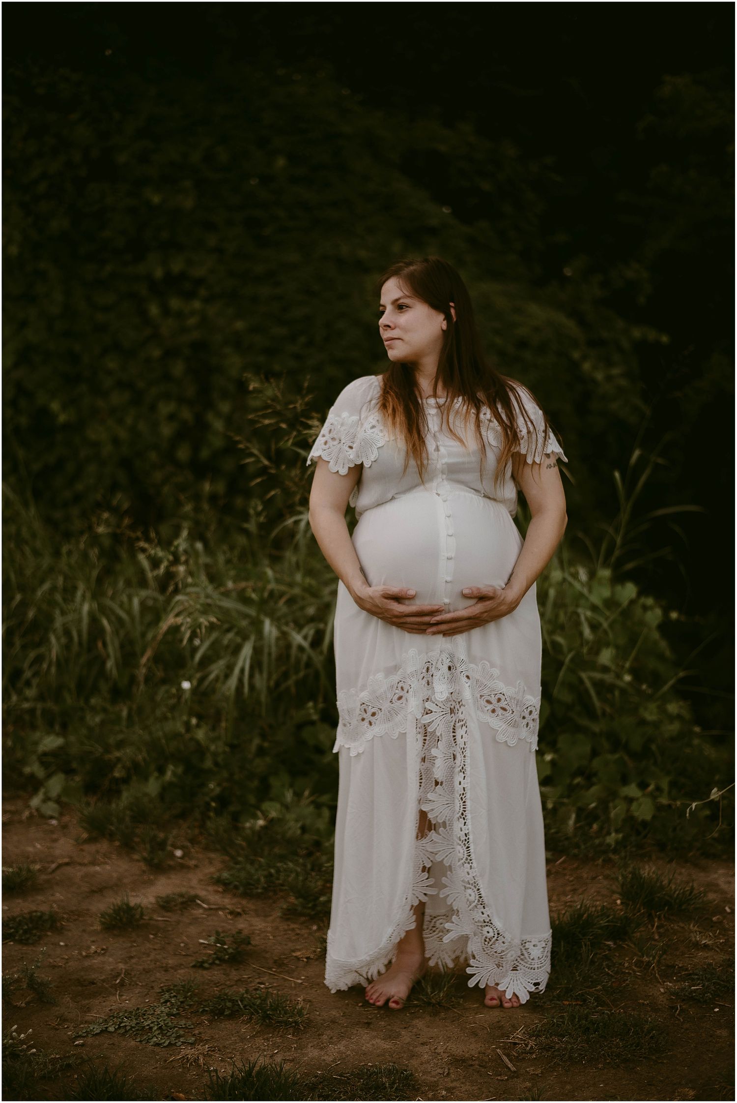 Artistic maternity photograph featuring intricate lace details against natural foliage.