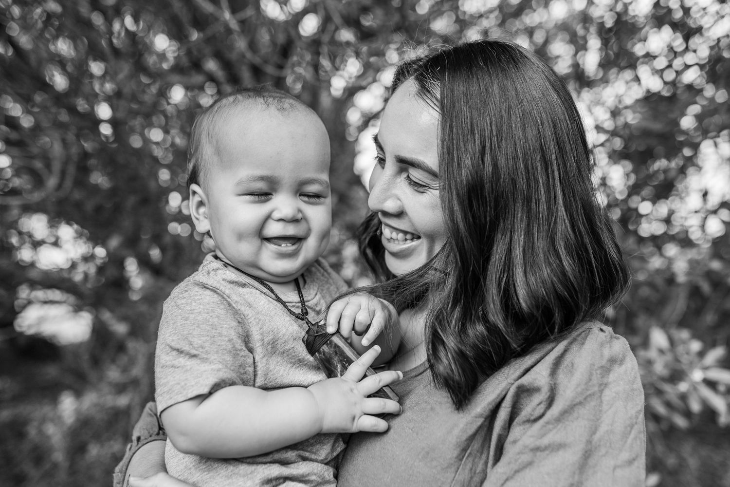 A black and white photograph capturing intimate laughter between parent and baby outdoors.