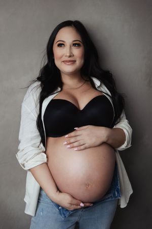 Professional maternity portrait in casual style against grey background.