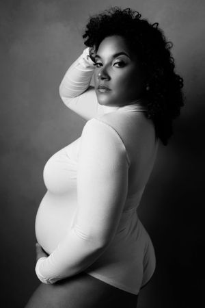 Dramatic black and white maternity portrait showing profile pose in fitted white top.