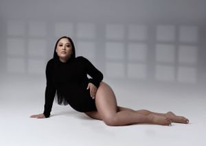 Artistic maternity pose in black bodysuit against white studio background.