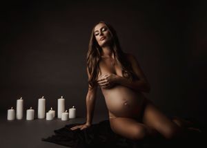 Artistic maternity portrait with candles in dark moody setting.