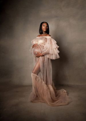 Ethereal maternity portrait in sheer ruffled dress against moody backdrop.