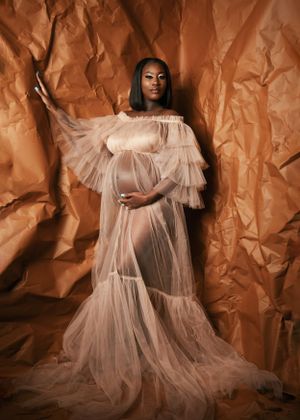 Dramatic maternity portrait with flowing white tulle gown against textured copper backdrop.